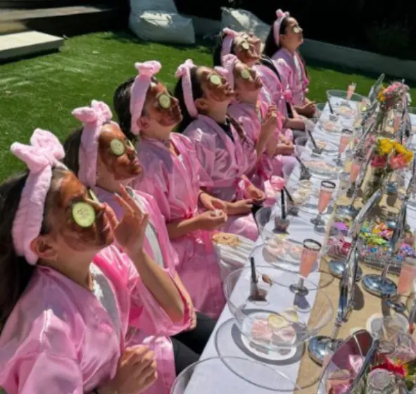 Spa day inspiration — kids in pink robes with face masks and cucumber slices at an outdoor spa table