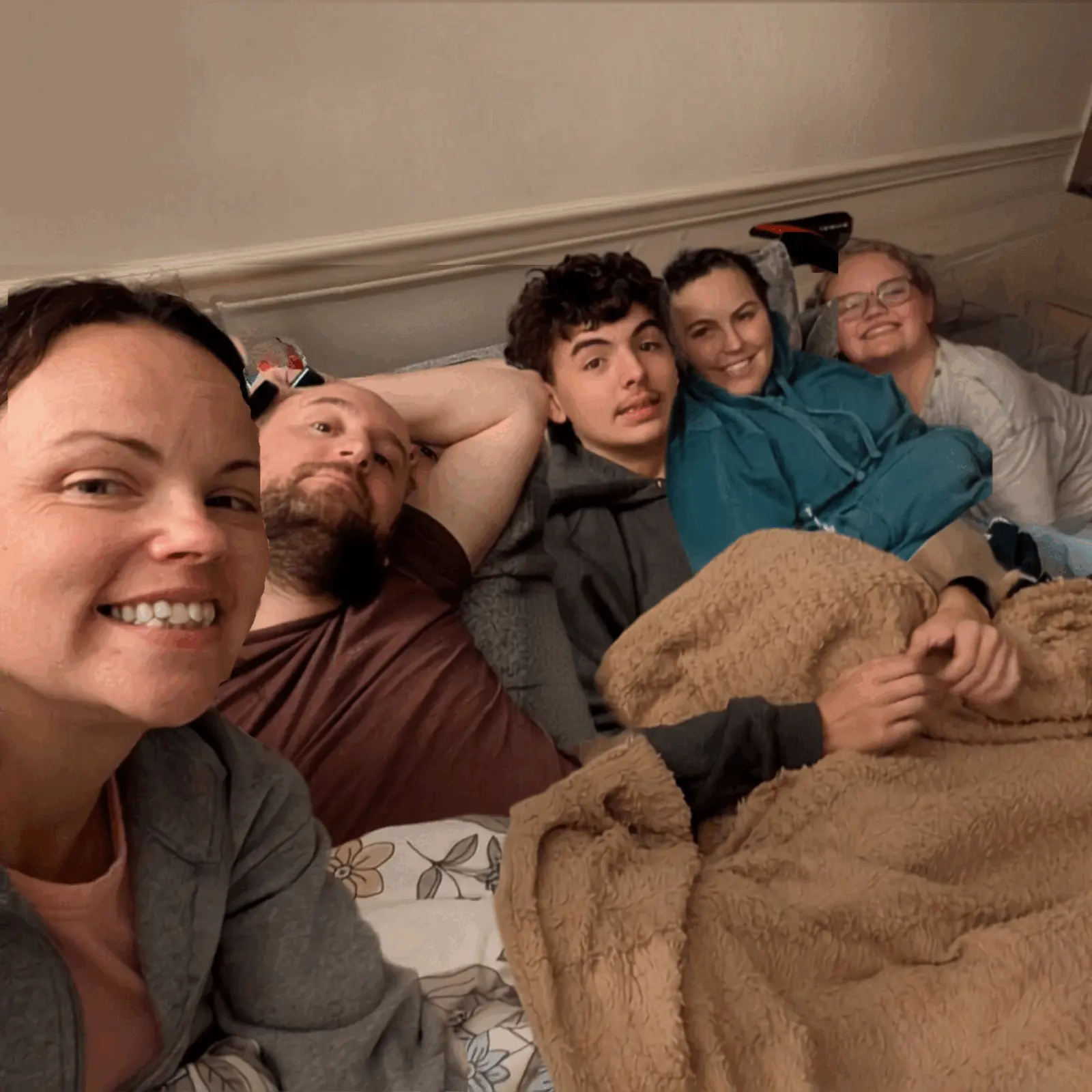 Real cozy gathering — group piled on bed with blankets