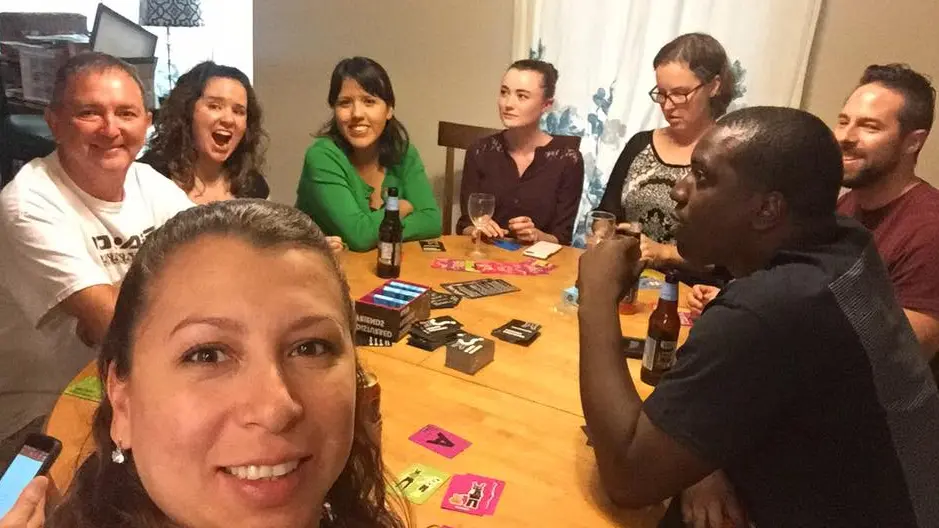 Real game night party — friends laughing and playing card games around a table