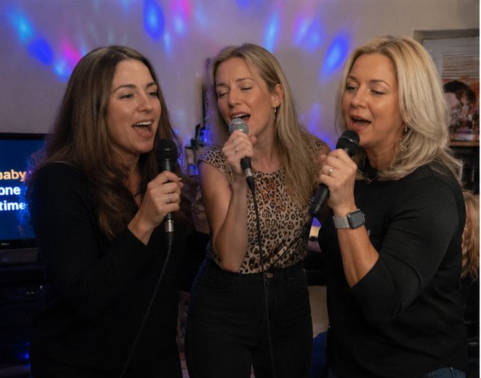 AI inspired karaoke party — three women sharing microphones under colorful party lights