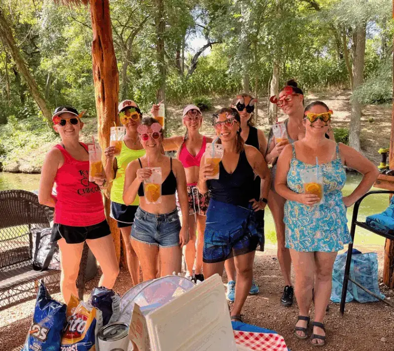Real luau party — group of women with tropical sunglasses and drinks outdoors by a river