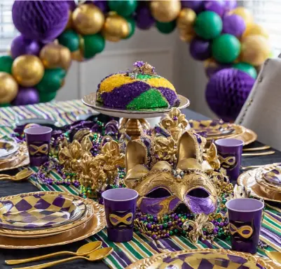 Mardi Gras inspiration — festive table with king cake, gold mask centerpiece, purple cups, and beads