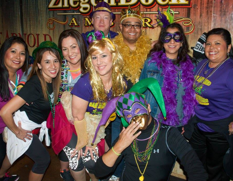 Real Mardi Gras party — group of friends in purple gold and green costumes with jester hats and feather boas at a bar