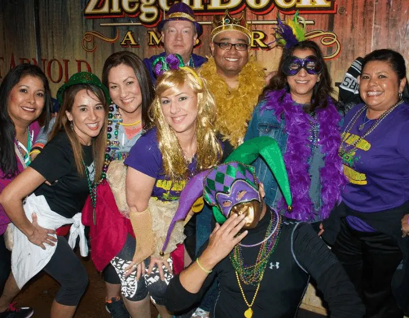 Real Mardi Gras party — group of friends in purple gold and green costumes with jester hats and feather boas at a bar