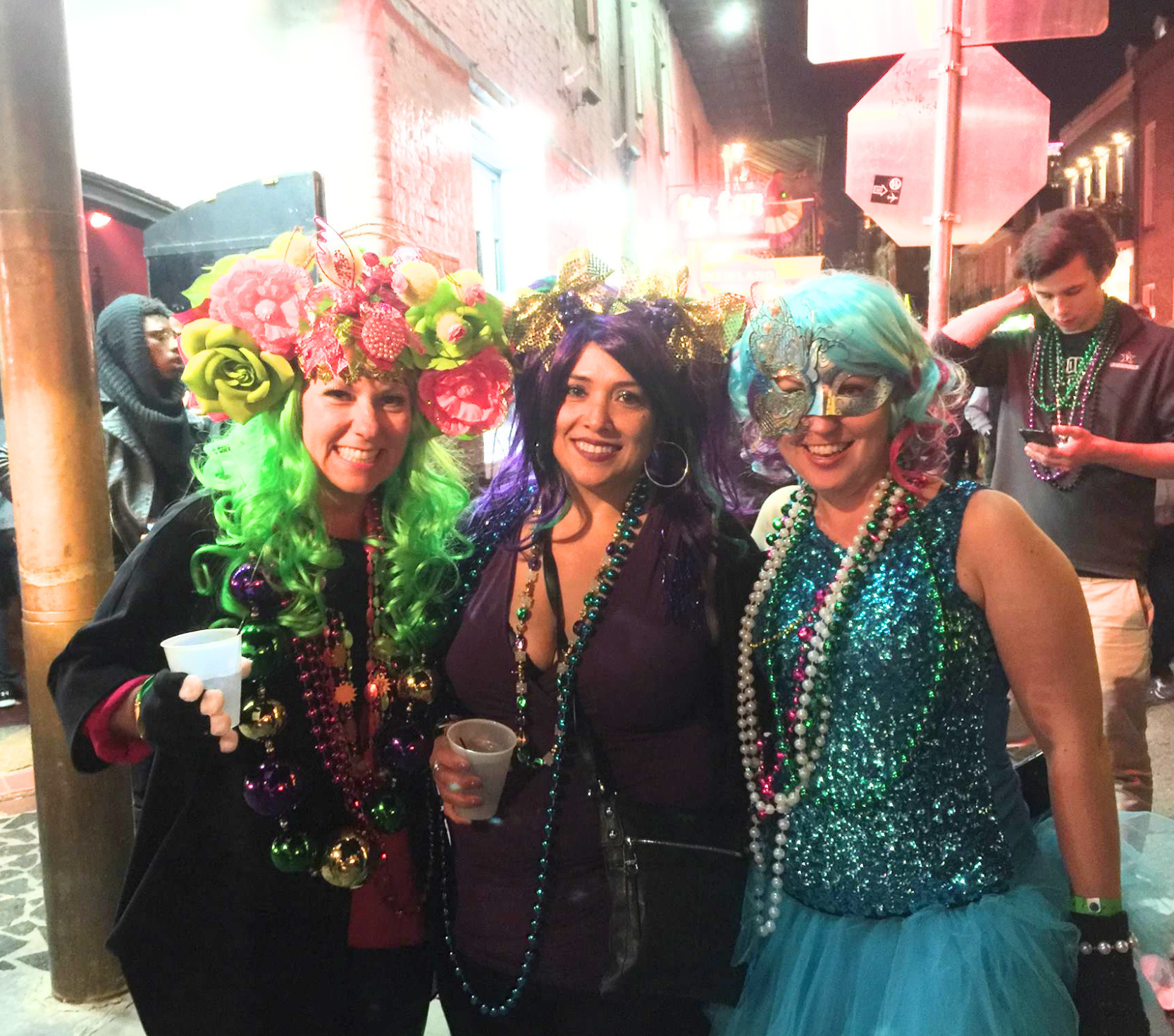 Real Mardi Gras party — three women in colorful wigs and beads on a New Orleans street at night