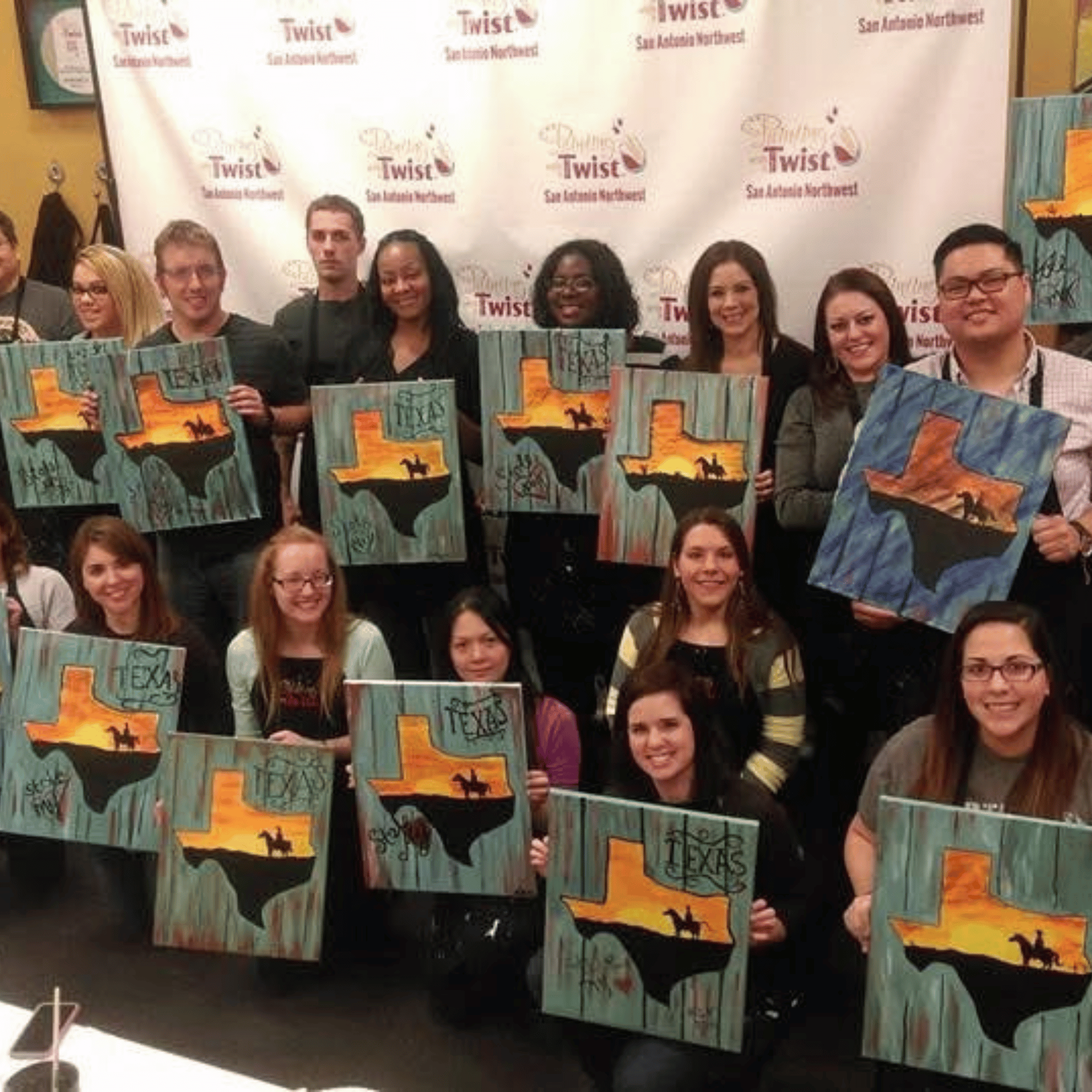Real paint and sip party — large group holding completed Texas paintings at Painting with a Twist