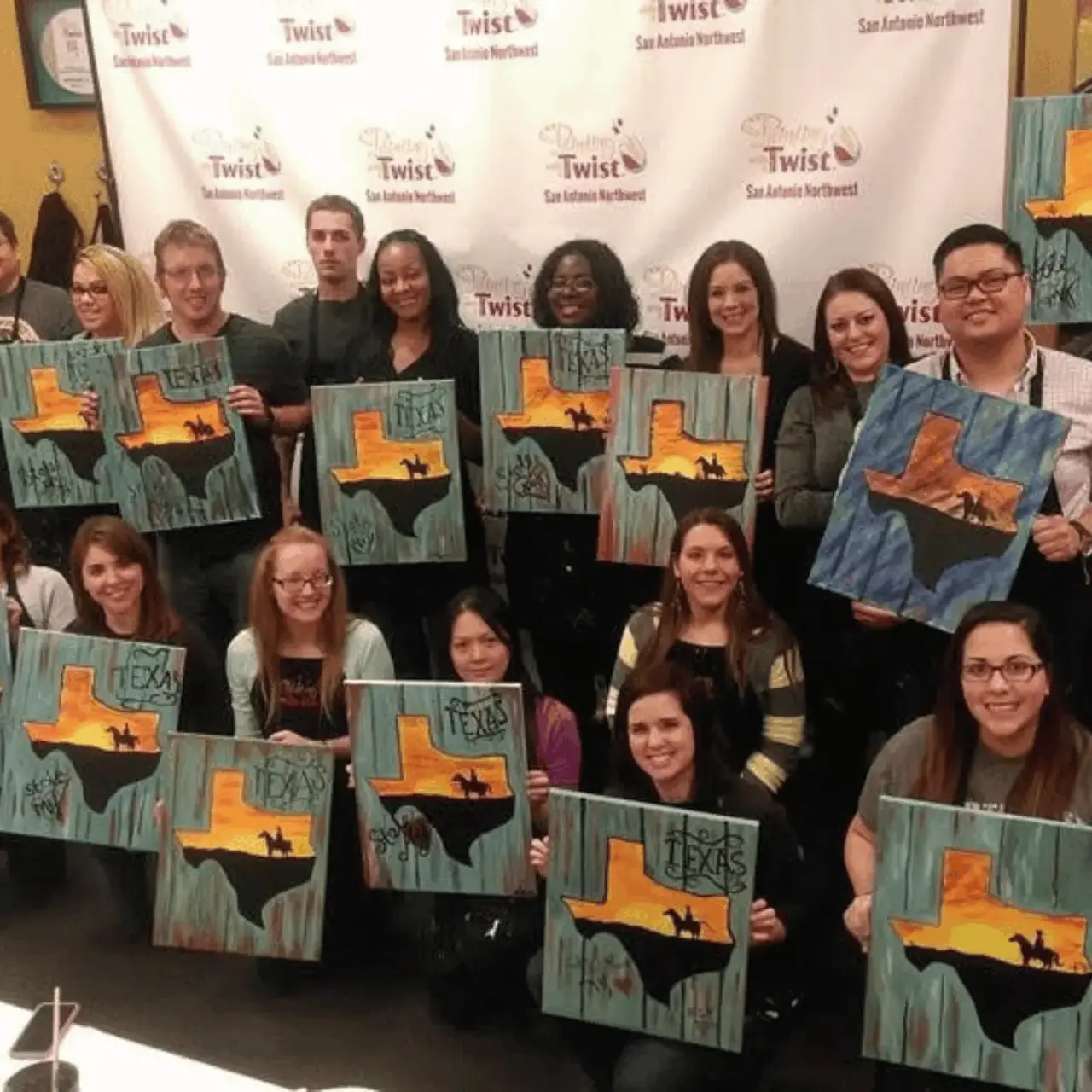 Real paint and sip party — guests holding their completed paintings