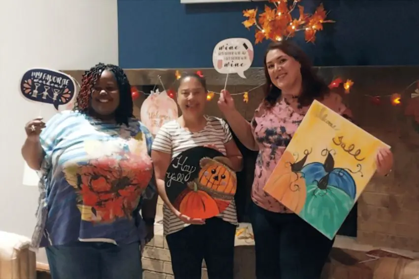 Real paint and sip party — three friends showing off their autumn pumpkin paintings