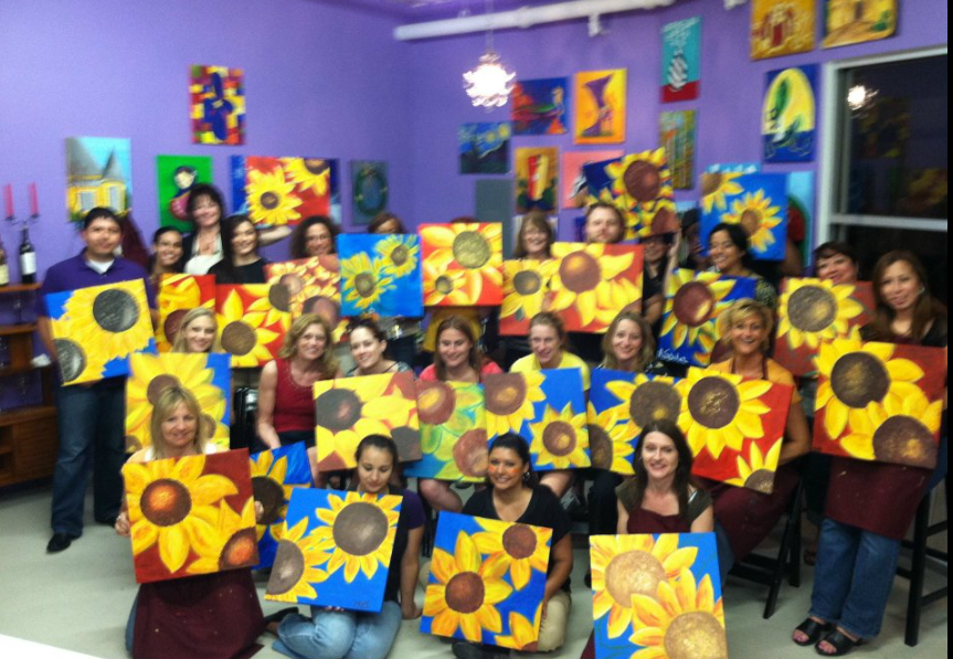 Real paint and sip party — large group holding sunflower paintings in a purple studio