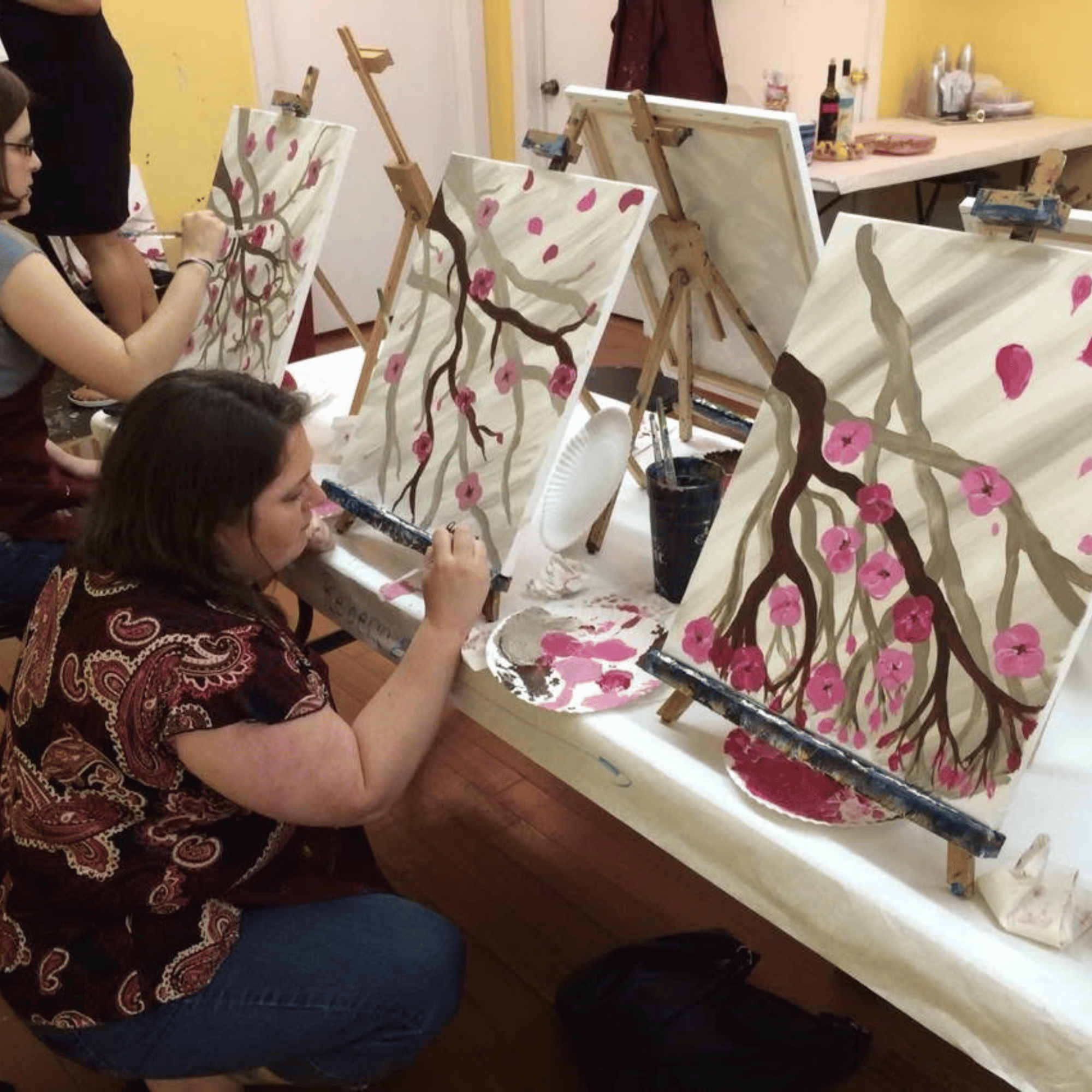 Real paint and sip party — woman painting cherry blossom canvas at an easel