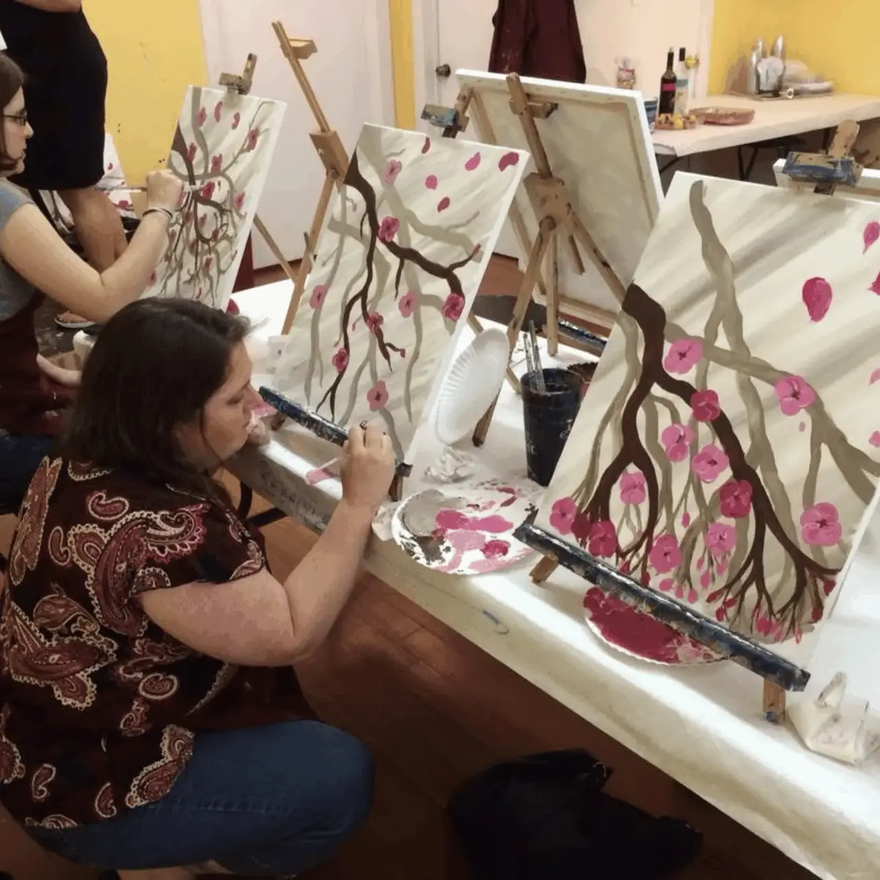 Real paint and sip party — woman painting cherry blossom canvas at an easel